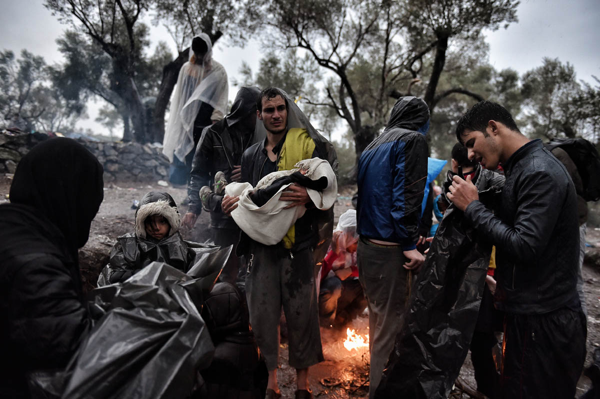 Migrants wait under an heavy rain, outside the Moria registration camp, on October 23, 2015, on the Lesbos island. Many Syrian families with small children are currently forced to walk a distance longer than the Athens Marathon from the beaches where they land to the points of registration near the port capital of Mytilene. Buses provided by local authorities and rides by volunteers do not suffice, especially as many refugees continue to land at night. Over 400,000 people have landed on Greek islands from neighbouring Turkey since the beginning of the year, most of them fleeing the civil war in Syria. AFP PHOTO / ARIS MESSINIS / AFP PHOTO / ARIS MESSINIS